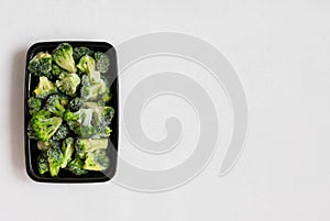 Frozen broccoli. Frozen vegetables in a plastic container on a white background. Food preparations for the freezer. Copy space,