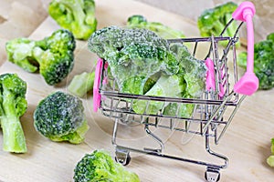Frozen broccoli in the shopping cart on light wooden background. Vegetable preservation and grocery buying concept.