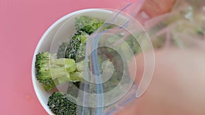 Frozen broccoli in white bowl on pink background top view.