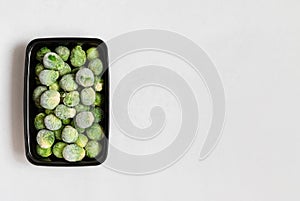 Frozen brussels sprouts in container on a white background. Frozen vegetables. Homemade preparations. View from above. Copy space