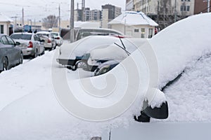 Frozen car covered snow at winter day, view front window windshield and hood on snowy background