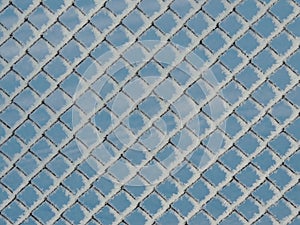 A frozen chain-link fence covered with snow in a sunny winter day