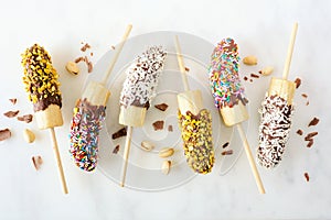 Frozen chocolate dipped banana pops, top view scattered on white marble