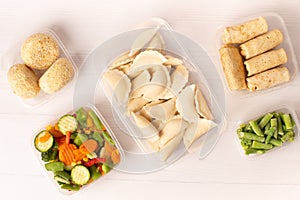 Frozen convenience foods and vegetables in plastic containers on a white table