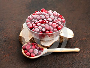 Frozen cranberries in a bowl and wooden spoon on a brown background. Frozen healthy food