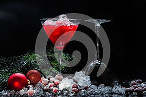 Frozen cranberries in sugar on a dark background in a cocktail glass and a glass of red cocktail on cranberry juice