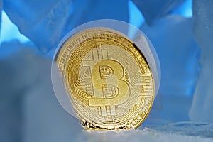 Frozen crypto currency bitcoin face obverse stands surrounded by blue ice in beautiful light.