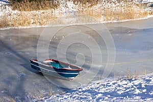Frozen ditch with wooden row-boat lying on the ice