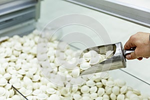 Frozen dumplings in an iron scoop in a woman's hand in a supermarket. Convenient semi-finished products. Close-up