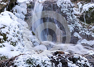 Frozen fast flowing spring water, icy rocks and water stream, frosty tree roots, beautiful ice and water texture