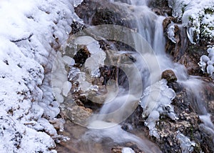 Frozen fast flowing spring water, icy rocks and water stream, frosty tree roots, beautiful ice and water texture