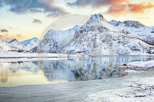 Frozen Flakstadpollen and Boosen fjords with red rorbuers and reflection in water during sunrise with Hustinden mountain on photo