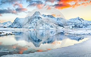 Frozen Flakstadpollen and Boosen fjords with red rorbuers and reflection in water during sunrise with Hustinden mountain on photo