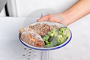 Frozen food. Hands are taking a plate of frozen cutlets and vegetables out of the freezer of the fridge