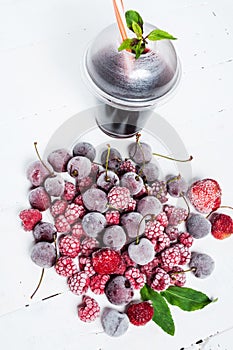 Frozen forest berries and cocktail in ice cubes on wooden table background.