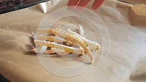 Frozen french fries are laid out by hand on a kitchen baking sheet for cooking in the oven. Slow motion close up view
