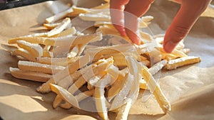 Frozen french fries are laid out by hand on a kitchen baking sheet for cooking in the oven. Slow motion close up view