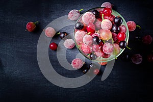 Frozen and fresh berries in a glass pial on a black background.