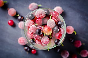 Frozen and fresh berries in a glass pial on a black background.