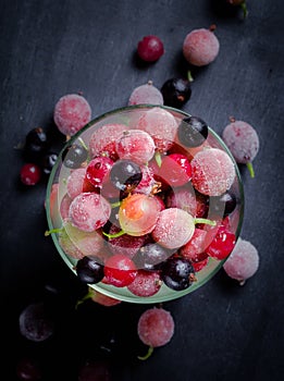 Frozen and fresh berries in a glass pial on a black background.