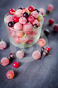 Frozen and fresh berries in a glass pial on a black background.