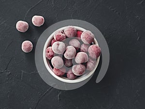 Frozen fresh farm cherry berries in white bowl on black background. Close-up. Top view