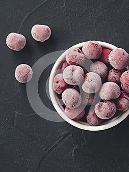 Frozen fresh farm cherry berries in white bowl on black background. Close-up. Top view