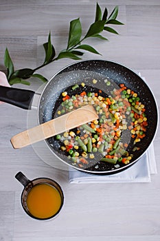 Frozen fried vegetables on black pan. Vegan breakfast with juice. Vegetables food mix on white wooden background with plant