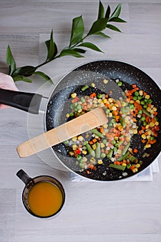 Frozen fried vegetables on black pan. Vegan breakfast with juice. Vegetables food mix on white wooden background with plant