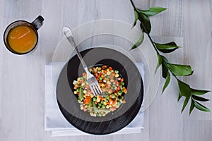 Frozen fried vegetables on black plate. Vegan breakfast with juice. Vegetables food mix on white wooden background with plant