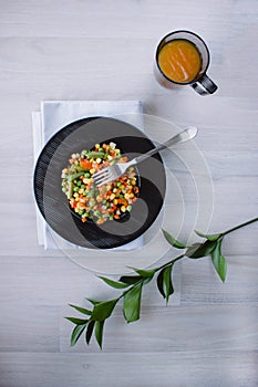 Frozen fried vegetables on black plate. Vegan breakfast with juice. Vegetables food mix on white wooden background with plant