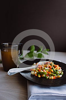 Frozen fried vegetables on black plate. Vegan breakfast with juice. Vegetables food mix on white wooden background with plant