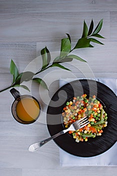 Frozen fried vegetables on black plate. Vegan breakfast with juice. Vegetables food mix on white wooden background with plant