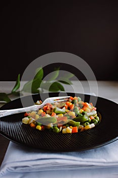 Frozen fried vegetables on black plate. Vegan breakfast. Vegetables food mix on white wooden background with plant