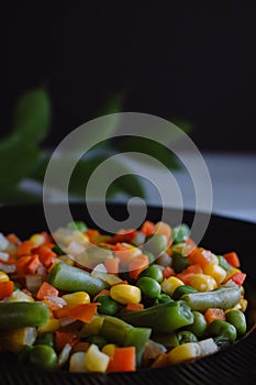 Frozen fried vegetables on black plate. Vegan breakfast. Vegetables food mix on white wooden background with plant