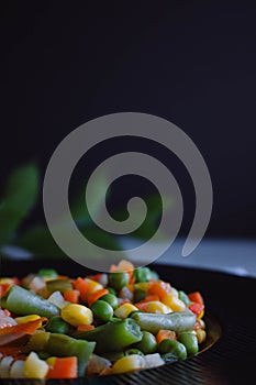 Frozen fried vegetables on black plate. Vegan breakfast. Vegetables food mix on white wooden background with plant