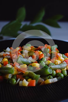 Frozen fried vegetables on black plate. Vegan breakfast. Vegetables food mix on white wooden background with plant