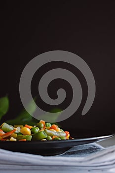 Frozen fried vegetables on black plate. Vegan breakfast. Vegetables food mix on white wooden background with plant