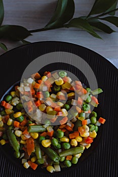 Frozen fried vegetables on black plate. Vegan breakfast. Vegetables food mix on white wooden background with plant