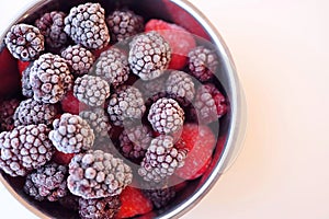 Frozen fruit berries in a pot on white background. Close-up with dark purple blackberries and red strawberries and raspberries.