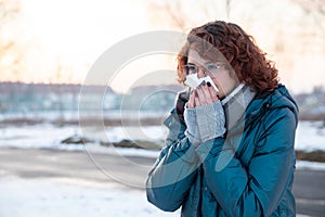 A frozen girl with glasses wipes her nose in a tissue.