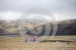 Frozen grassland with single house and misty hills behind on Tibetan Plateau