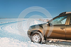 Frozen And Grungy SUV Car Parked On Winter Snowy Field Countryside Landscape. Altered Sky With Plane