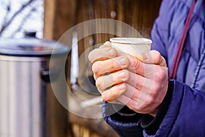 Frozen hands hold a disposable paper cup with hot tea. Warming in cold winter. Selective focus. Background