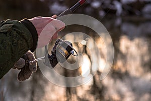 The frozen hands of a male angler holding a spinning reel wind a fishing line on a reel against the background of the