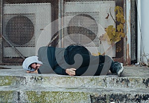 Frozen homeless man sleeps on concrete near building's ventilation system. Problem of how homeless survive winter