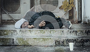 Frozen homeless man sleeps on concrete near building's ventilation system. Problem of how homeless survive winter