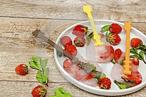Frozen ice with red strawberry, mint in guitar shape for cold fresh summer lemonade cocktail drinks. Homemade sweet fruit berry