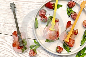 Frozen ice with red strawberry, mint in guitar shape for cold fresh summer lemonade cocktail drinks. Homemade sweet fruit berry