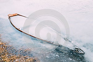 Frozen into ice of river, lake, pond old wooden boat. Forsaken r